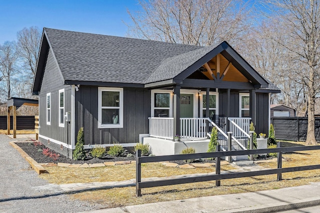 bungalow-style home with board and batten siding, covered porch, roof with shingles, and fence