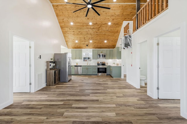 kitchen with stainless steel appliances, green cabinetry, a towering ceiling, and wood finished floors