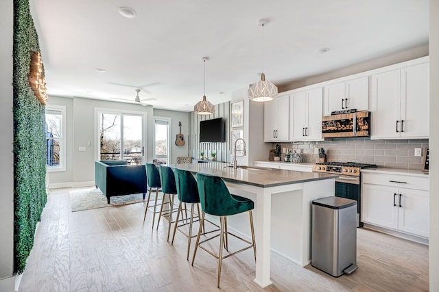 kitchen featuring decorative light fixtures, sink, white cabinets, a kitchen island with sink, and stainless steel appliances