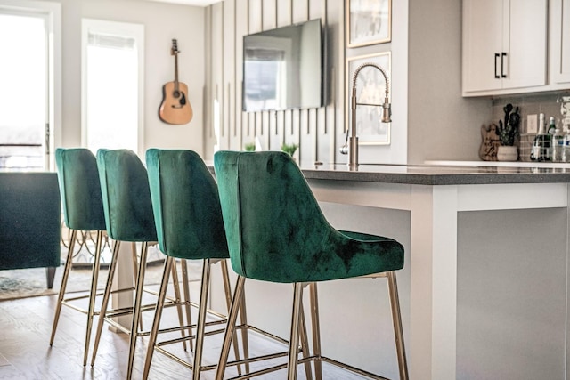 bar with white cabinetry, sink, light hardwood / wood-style floors, and decorative backsplash