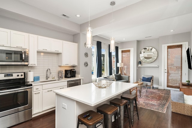 kitchen with pendant lighting, white cabinetry, sink, a kitchen bar, and stainless steel appliances