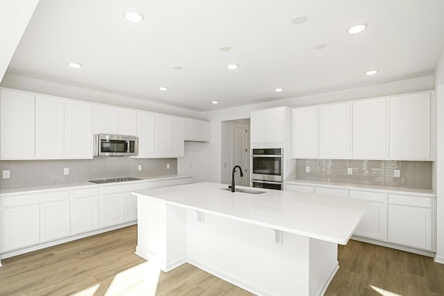 kitchen featuring sink, stainless steel appliances, white cabinets, and a center island with sink