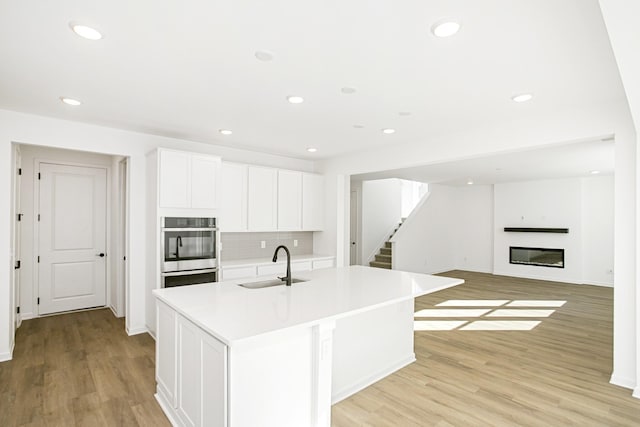 kitchen with sink, white cabinetry, light hardwood / wood-style flooring, a kitchen island with sink, and decorative backsplash