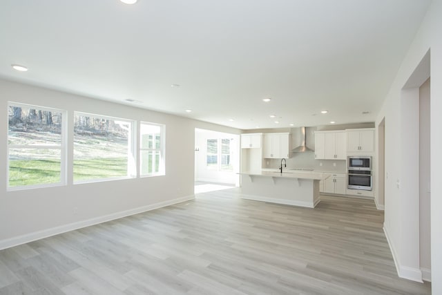 kitchen with an island with sink, white cabinetry, sink, stainless steel appliances, and wall chimney exhaust hood