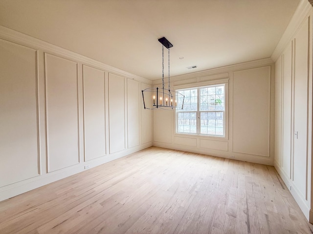 spare room featuring a chandelier, light wood-style flooring, a decorative wall, visible vents, and crown molding