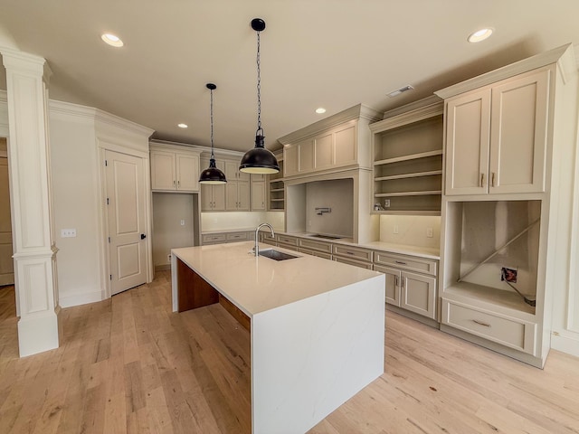 kitchen featuring light countertops, a center island with sink, open shelves, decorative columns, and pendant lighting