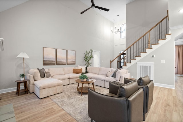 living room with ceiling fan with notable chandelier, light hardwood / wood-style flooring, and a high ceiling