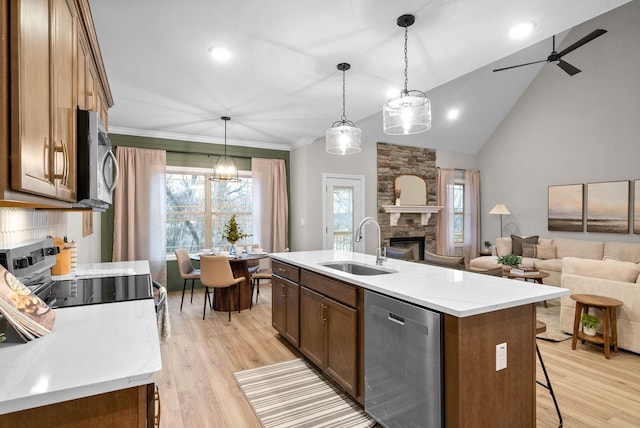 kitchen featuring sink, stainless steel appliances, a fireplace, a center island with sink, and decorative light fixtures