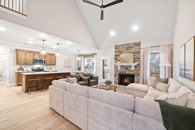 living room with a stone fireplace, high vaulted ceiling, ornamental molding, ceiling fan, and light wood-type flooring