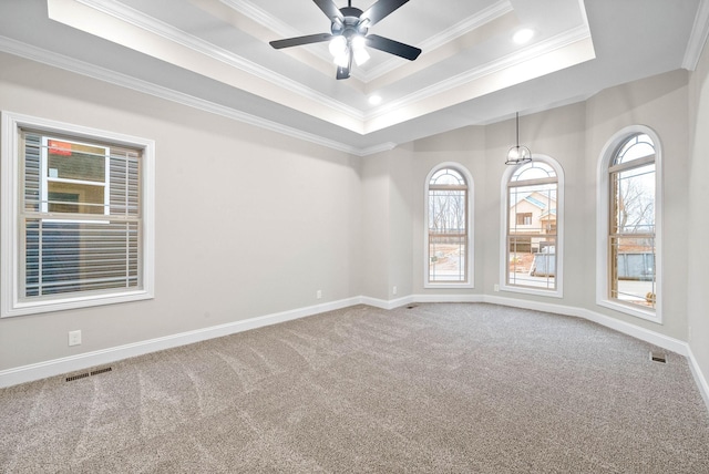 carpeted spare room with ceiling fan, ornamental molding, a healthy amount of sunlight, and a raised ceiling