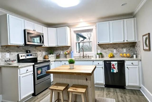 kitchen with sink, a breakfast bar area, white cabinetry, appliances with stainless steel finishes, and hardwood / wood-style floors