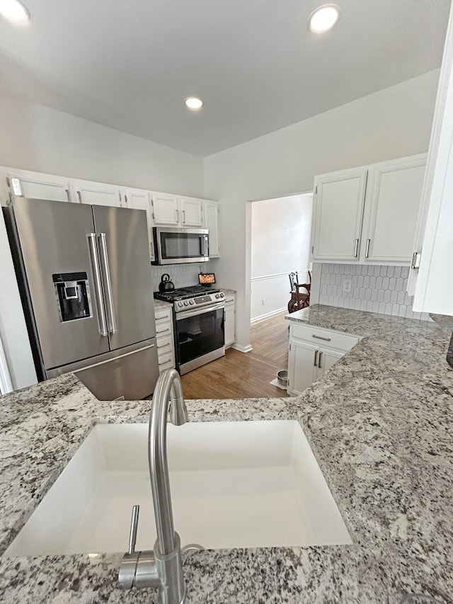 kitchen featuring backsplash, light stone countertops, white cabinets, and appliances with stainless steel finishes