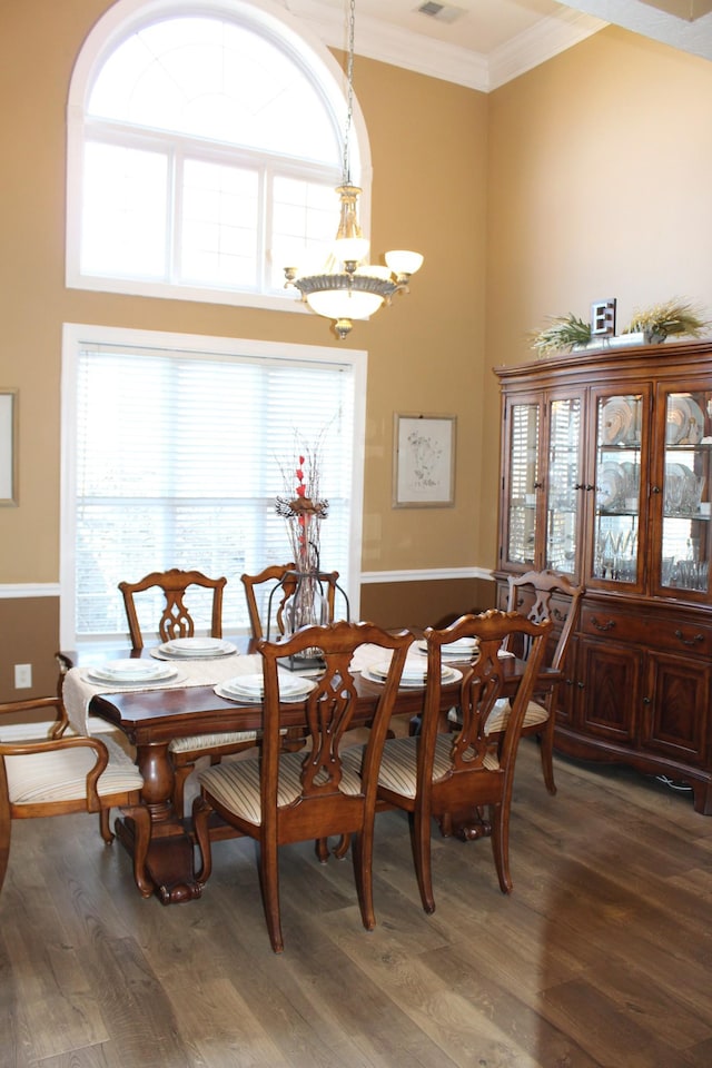 dining space featuring visible vents, ornamental molding, wood finished floors, a high ceiling, and a chandelier