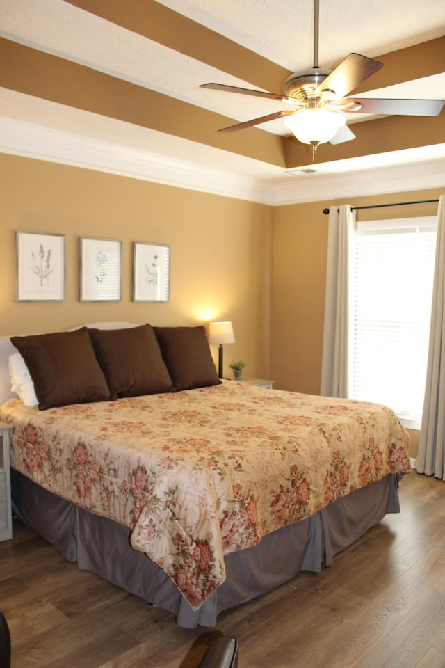 bedroom with a tray ceiling, crown molding, and wood finished floors