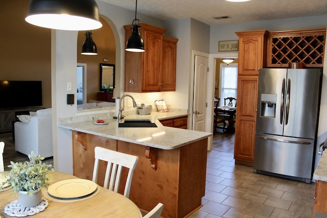 kitchen featuring arched walkways, stainless steel fridge with ice dispenser, a sink, a peninsula, and a kitchen bar