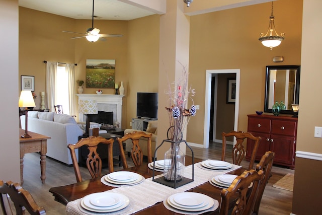 dining area featuring ceiling fan, a high ceiling, a fireplace, and wood finished floors