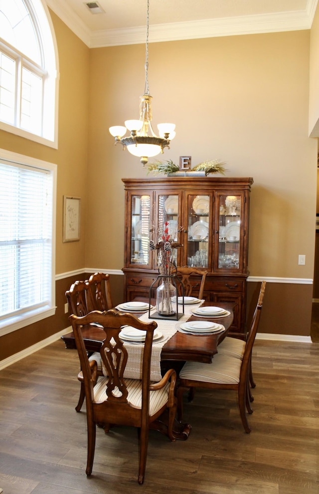 dining space with crown molding, a notable chandelier, a towering ceiling, wood finished floors, and baseboards