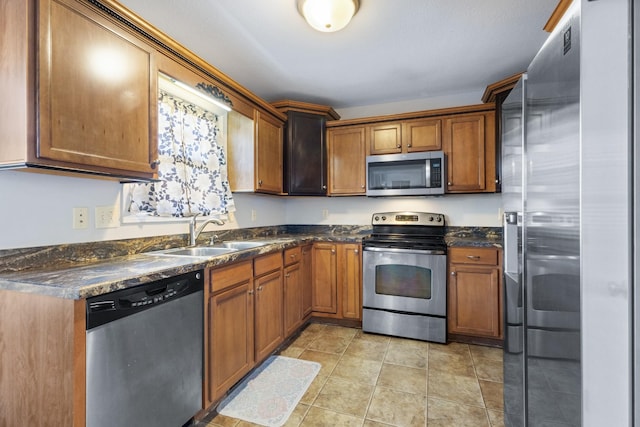 kitchen with dark stone countertops, sink, light tile patterned floors, and stainless steel appliances