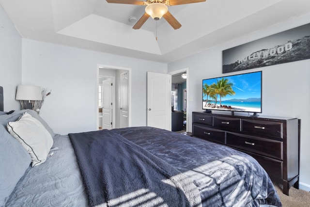 bedroom with a tray ceiling, ensuite bathroom, ceiling fan, and carpet