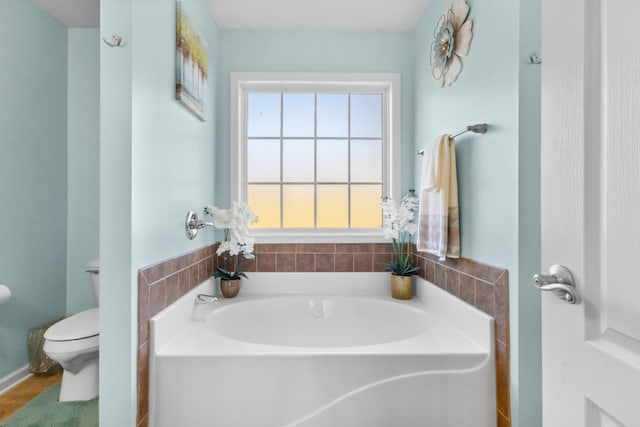 bathroom with a tub to relax in and toilet