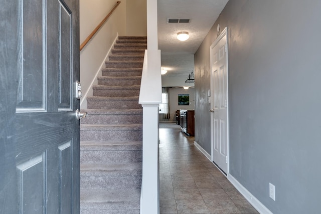 stairs with tile patterned floors and a textured ceiling