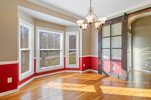 unfurnished dining area with ornamental molding, hardwood / wood-style flooring, a notable chandelier, and a barn door