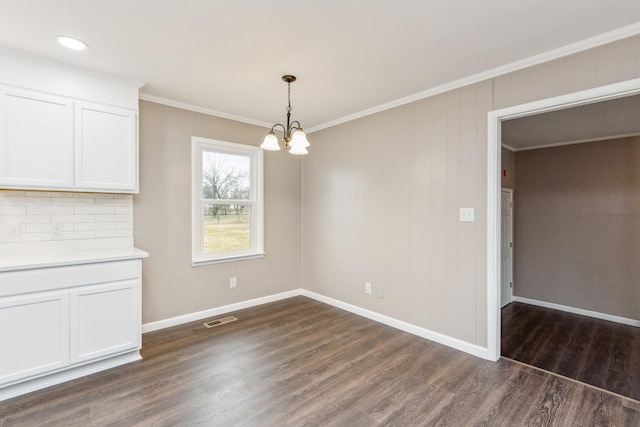 unfurnished dining area with crown molding, dark wood-type flooring, and an inviting chandelier