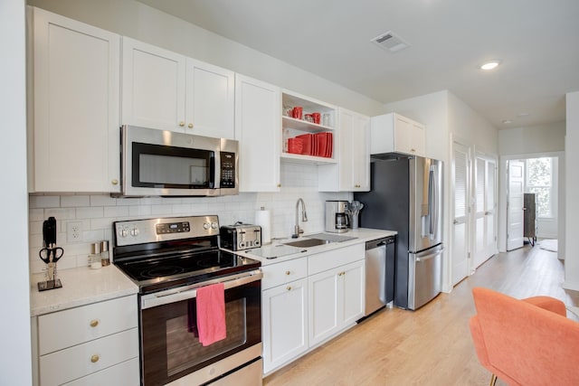 kitchen with appliances with stainless steel finishes, tasteful backsplash, sink, white cabinets, and light hardwood / wood-style floors