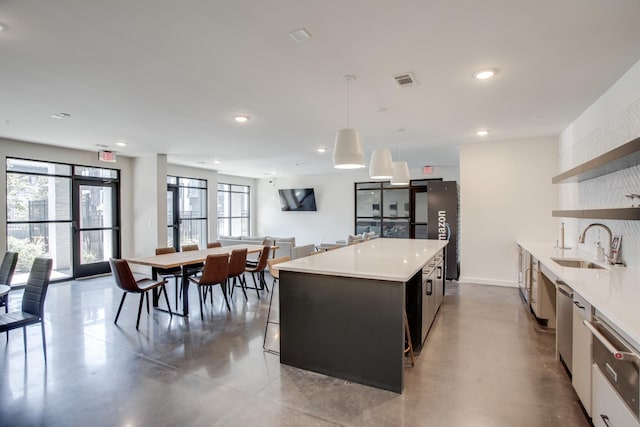 kitchen featuring concrete flooring, a wealth of natural light, decorative light fixtures, sink, and a center island