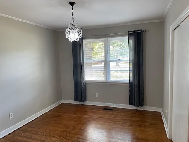 unfurnished room with an inviting chandelier, crown molding, and dark wood-type flooring