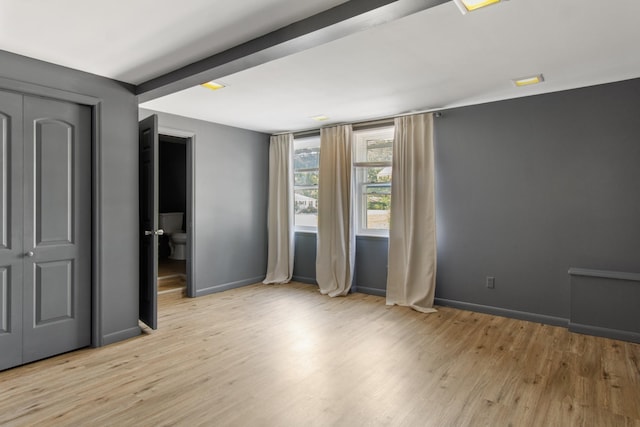 unfurnished bedroom with beam ceiling and light hardwood / wood-style floors