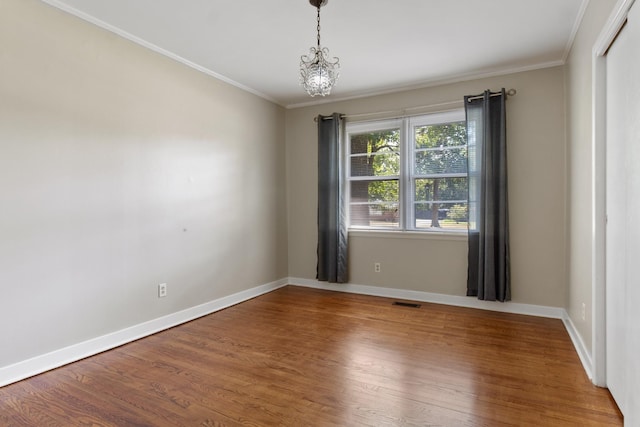 spare room featuring hardwood / wood-style floors, ornamental molding, and a chandelier