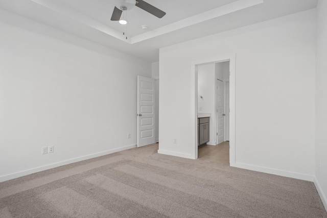 unfurnished bedroom featuring ensuite bathroom, light colored carpet, ceiling fan, and a tray ceiling