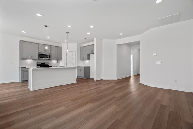 kitchen with sink, dark wood-type flooring, gray cabinetry, stainless steel appliances, and an island with sink