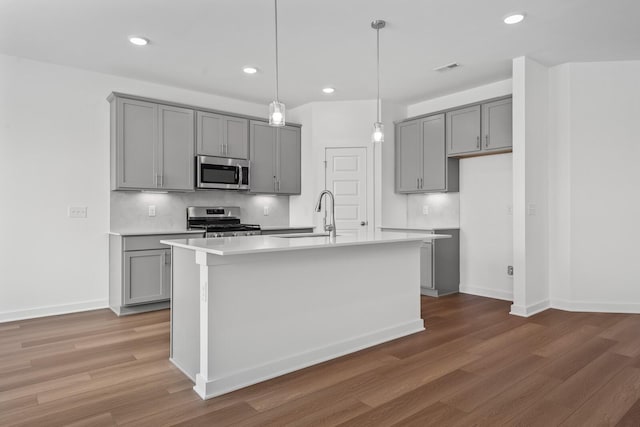 kitchen with sink, appliances with stainless steel finishes, gray cabinetry, a center island with sink, and decorative light fixtures