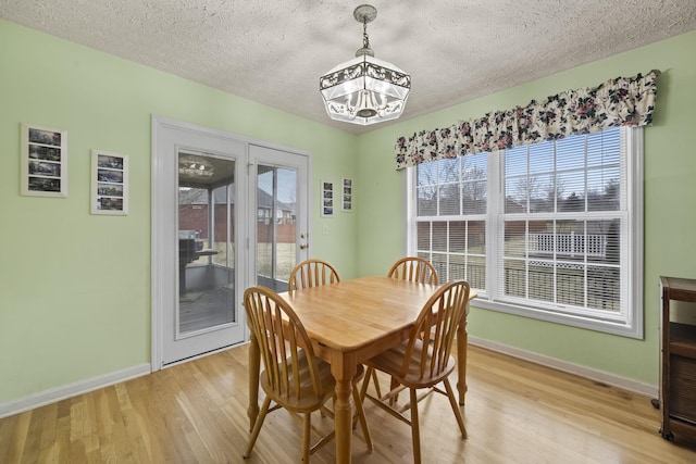 dining area with an inviting chandelier, a wealth of natural light, a textured ceiling, and light wood-type flooring