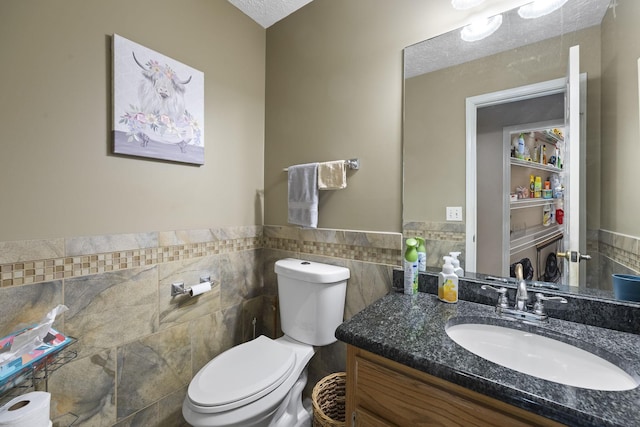 bathroom featuring vanity, toilet, tile walls, and a textured ceiling