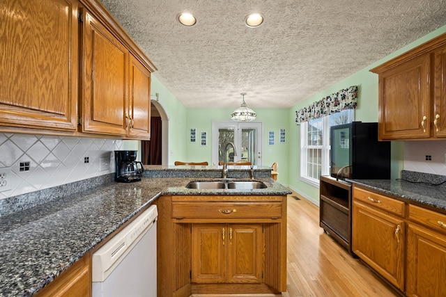 kitchen with pendant lighting, sink, black refrigerator, white dishwasher, and light wood-type flooring