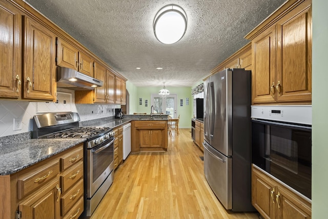 kitchen featuring appliances with stainless steel finishes, tasteful backsplash, sink, kitchen peninsula, and light wood-type flooring