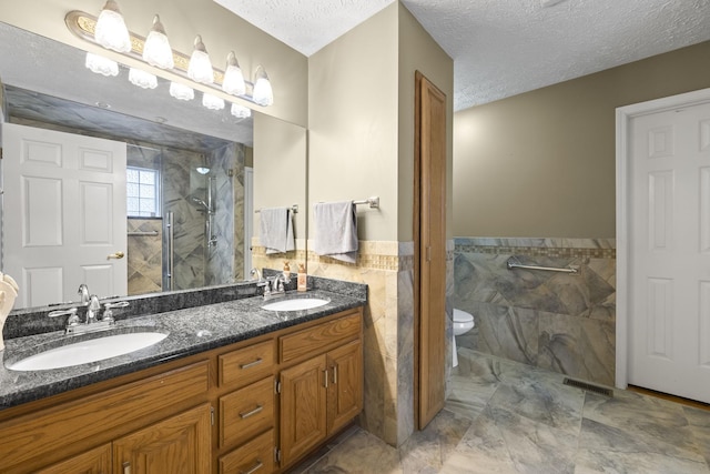 bathroom with tile walls, vanity, walk in shower, toilet, and a textured ceiling