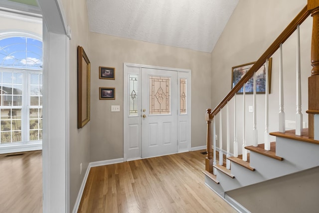 foyer entrance with lofted ceiling, a textured ceiling, and light hardwood / wood-style flooring