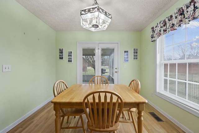 dining space with an inviting chandelier, a textured ceiling, light hardwood / wood-style flooring, and a healthy amount of sunlight