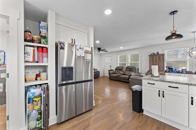 kitchen with pendant lighting, white cabinetry, stainless steel fridge, light stone counters, and light hardwood / wood-style flooring