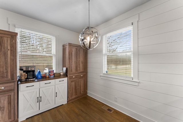 unfurnished dining area with a healthy amount of sunlight, an inviting chandelier, and dark hardwood / wood-style flooring