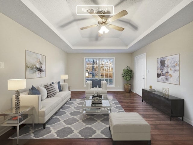 living room featuring ceiling fan, a tray ceiling, dark hardwood / wood-style flooring, and a textured ceiling