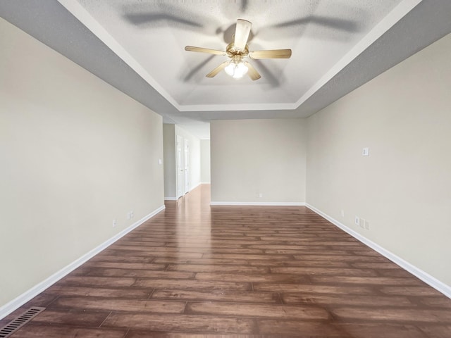 spare room with a tray ceiling, dark wood-type flooring, and ceiling fan