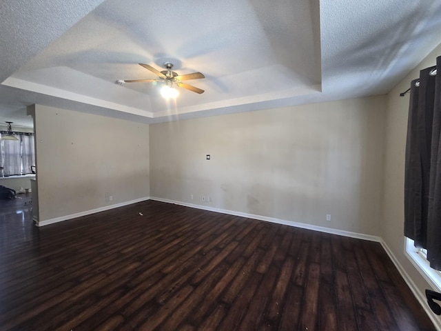 unfurnished room featuring dark wood-style floors, ceiling fan, a tray ceiling, and a textured ceiling