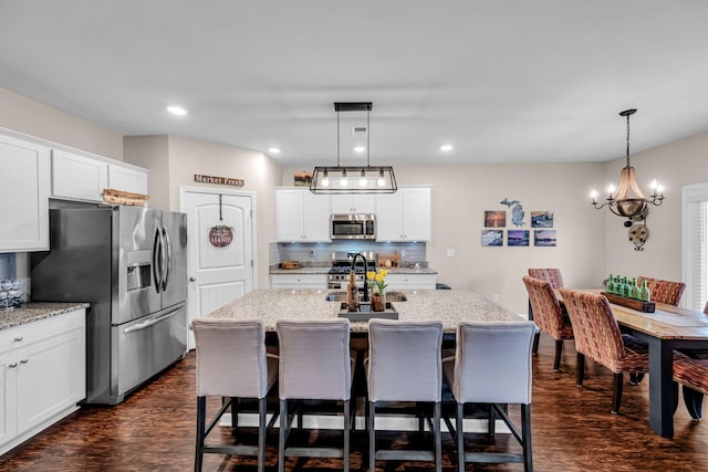 kitchen with a kitchen island with sink, hanging light fixtures, white cabinetry, and stainless steel appliances