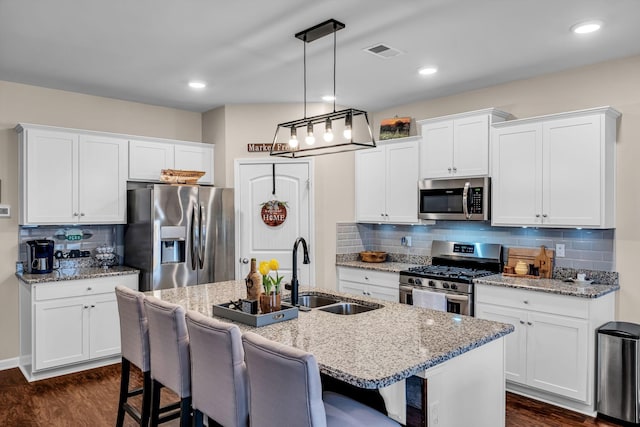 kitchen featuring pendant lighting, sink, stainless steel appliances, an island with sink, and white cabinets