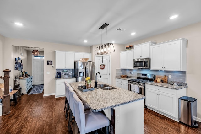 kitchen featuring sink, light stone counters, stainless steel appliances, a kitchen island with sink, and white cabinets